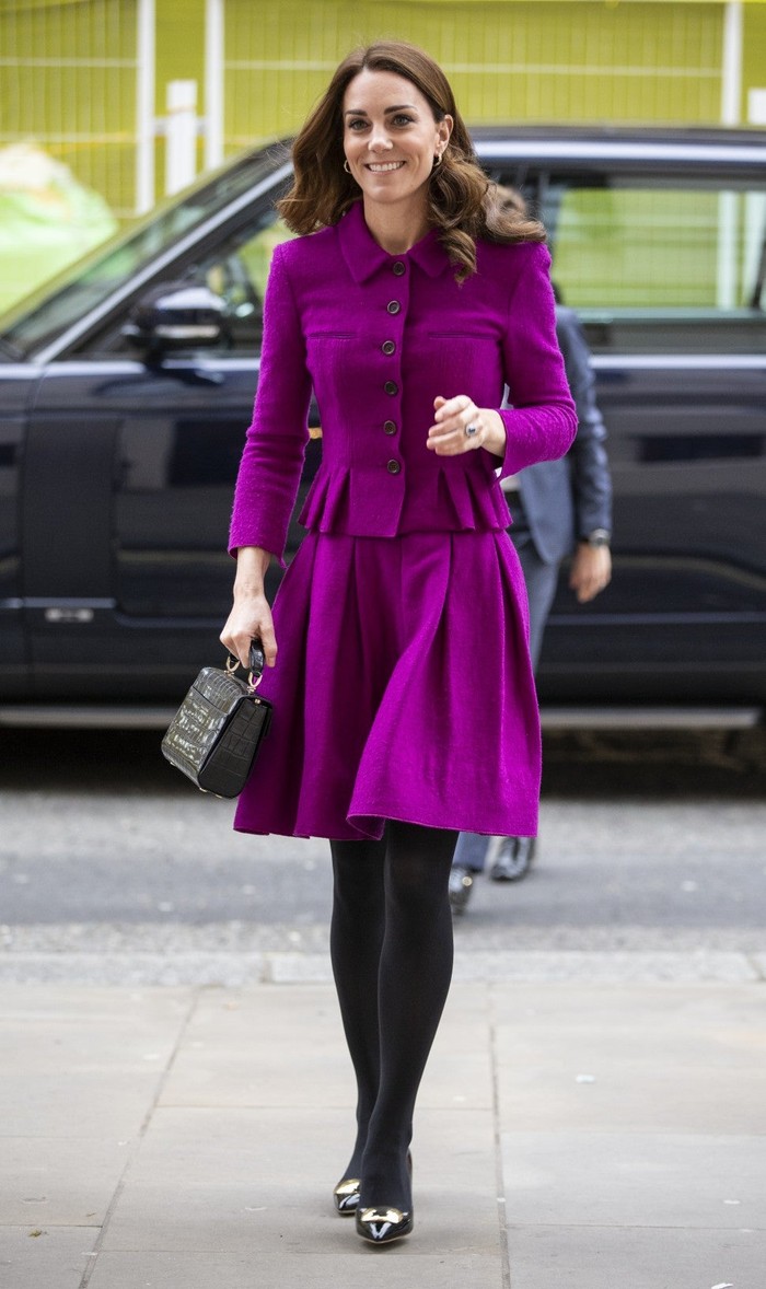 Kate tampil mengenakan skirt suit bewarna ungu terang saat kunjungi The Nook Children Hospice di Norfolk.Dengan stocking dan tas sebagai penambah penampilannya.(etonline.com)