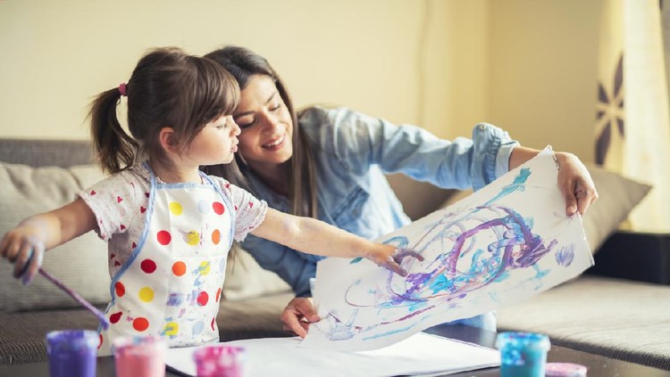 A young mother and her cute little daughter painting with colorful paints and having fun at home.