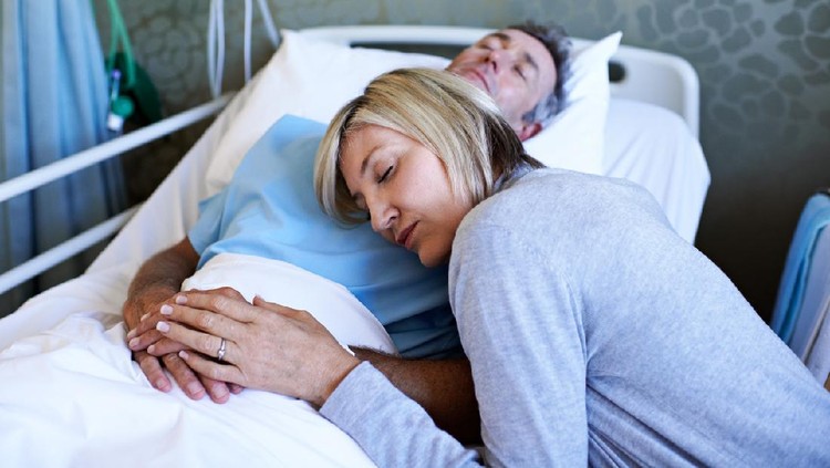 Shot of a wife comforting her husband asleep in a hospital bed