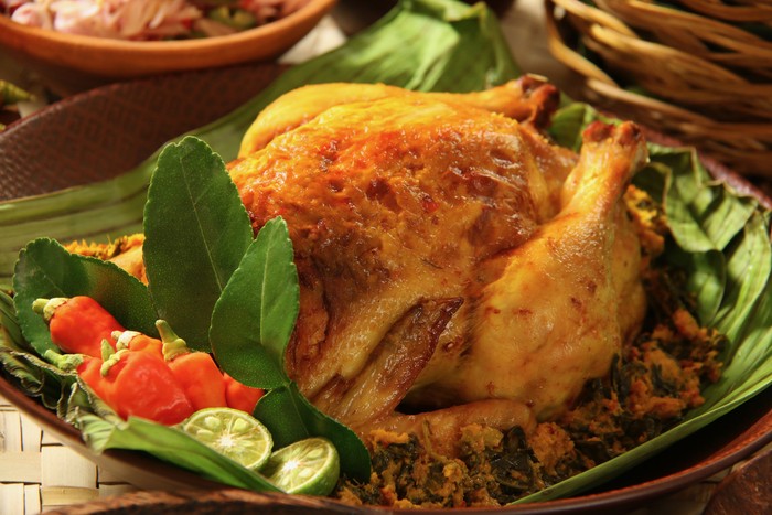 Ayam Betutu, the popular roast chicken dish from Bali. Stuffing of cassava and spices are stuffed inside the chicken. The chicken is garnished with kaffir lime leaves, red chili peppers and lime halves.