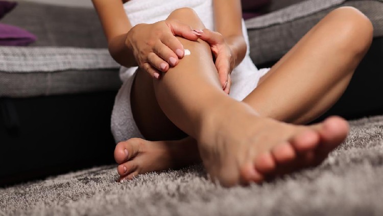 Ilustrasi selangkangan Woman smears cream on her leg at home on the floor. Girl wears white towel. Skincare and beauty concept