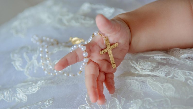 Nama Bayi Kristen Child's hand with a crucifix on a white cloth.