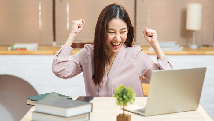 Smiling young entrepreneur Asian business woman working with internet using computer sit at apartment, Happy girl writing on notebook look at laptop screen listen and learning online courses