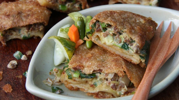 martabak telur Martabak Telor, or also known as Martabak Malabar, is a pan-fried pastry cake stuffed with egg, ground meat, green onion, and spices. Here the martabak has been cooked and cut into squares; two pieces are plated and accompanied with spicy cucumber pickle. A wooden fork is placed on the right hand side of the served martabak pieces. Further back in the background, some martabak pieces are shown in blur.