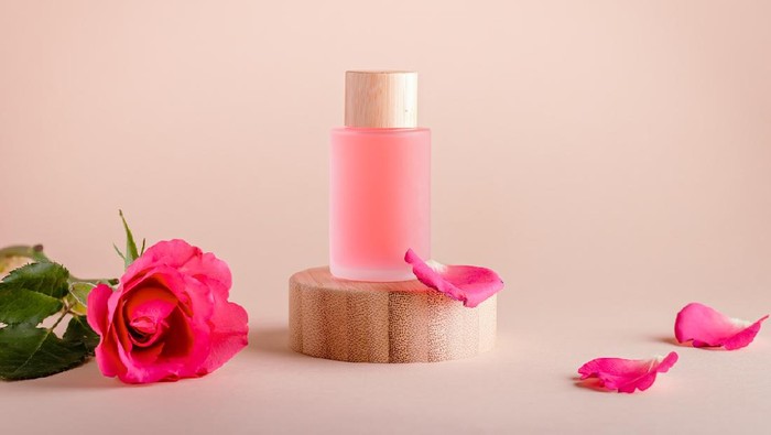 Rose extract facial serum in refillable bottles on wooden podium with rose flower, minimal composition