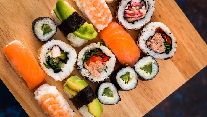 Close up macro color image depicting a delicious arrangement of fresh traditional Japanese sushi rolls topped with smoked salmon, prawn and avocado.
