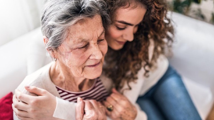 A teenage girl with grandmother at home, hugging. Family and generations concept.