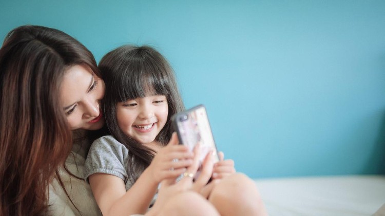 Ilustrasi Pemakaian Gadget Anak dengan Pengawasan Orang Tua Portrait Happy Daughter playing smartphone with her mother
