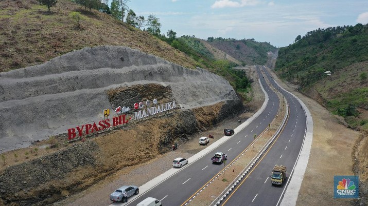 Foto udara menunjukkan pendendara melewati jalan Bypass Bil Mandalika, Lombok, Nusa Tenggara Barat, Kamis (4/1/2021).  Kementerian Pekerjaan Umum & Perumahan Rakyat (PUPR) melalui Badan Pengembangan Infrastruktur Wilayah (BPIW) membangun jalan elak atau bypass yang menghubungkan Bandara Internasional Lombok dengan Kawasan Pariwisata Mandalika sejauh 17 kilometer. Keberadaan jalan ini bakal mendukung aktivitas pariwisata di Mandalika seiring rencana penyelenggaraan balap motor MotoGP pada 2021 mendatang. Pembangunan jalan ini akan meningkatkan konektivitas dari Bandara BIL ke Kawasan Wisata Mandalika dan mendukung akses menuju sirkuit MotoGP yang dibangun di Kawasan Mandalika. Jalan ini juga akan mengurangi waktu tempuh dari BIL ke Mandalika menjadi 15 menit. Sebab, jika semula melewati jalan lama bisa lebih dari 45 menit.  Jalan Bypass BIL-Mandalika memiliki panjang 17,363 kilometer dengan lebar right of way (ROW) 50 meter serta 4 lajur yang dilengkapi median jalan. Menelan anggaran sekitar Rp 706 miliar pada 2020–2021. Pembangunannya terdiri dari tiga paket pekerjaan. Yakni Paket I sepanjang 4,30 km (STA 0+000-STA 4+300) dengan kontraktor PT Nindya Karya-Bumi Agung (KSO) dengan anggaran sebesar Rp199 miliar. Kemudian Paket 2 sepanjang 9,70 km (STA 4+300-STA 14+000) kontraktornya PT Adhi Karya (Persero) Tbk-PT Metro Lestari Utama (KSO) dengan anggaran senilai Rp 353 miliar. Selanjutnya untuk Paket 3 sepanjang 3,363 km (STA 14+00-STA 17+363), kontraktornya PT Yasa Patria Perkasa dengan anggaran senilai Rp 152 miliar.  (CNBC Indonesia/ Tri Susilo)