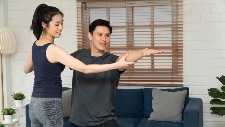 Healthy young Asian couple exercises in home and wife teaching her husband for exercise in COVID-19 quarantine at home. A new normal lifestyle and healthy exercise can be done anywhere.