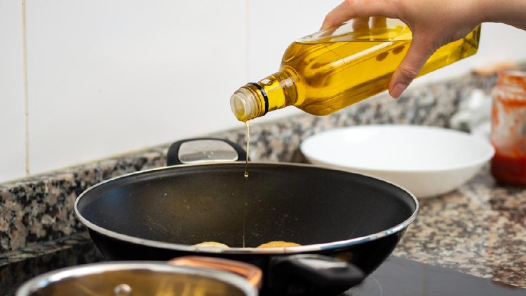 woman pouring cooking oil from bottle into frying pan on stove