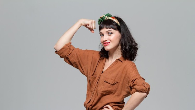 Beautiful positive happy young woman showing biceps isolated over grey background