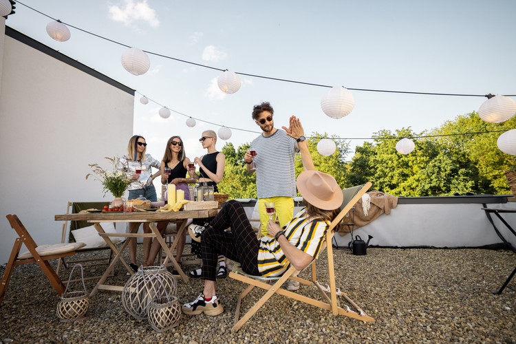Young group of stylish people having a festive dinner on the roof terrace. Hipsters hanging out and having great summertime together outdoors