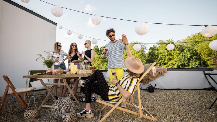Young group of stylish people having a festive dinner on the roof terrace. Hipsters hanging out and having great summertime together outdoors
