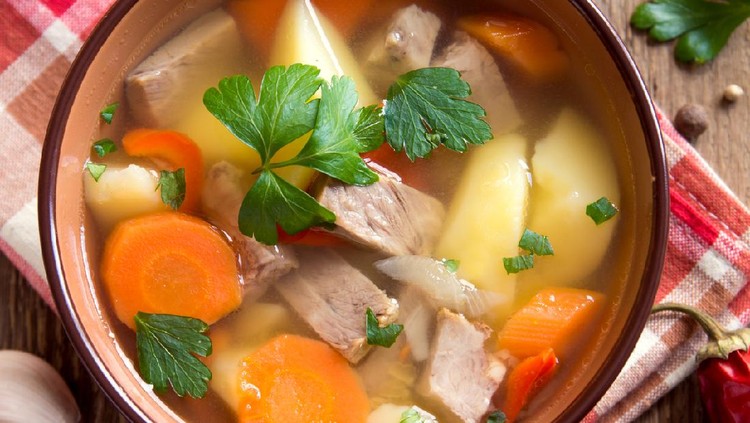 Meat and vegetables soup with parsley in bowl over rustic wooden background close up