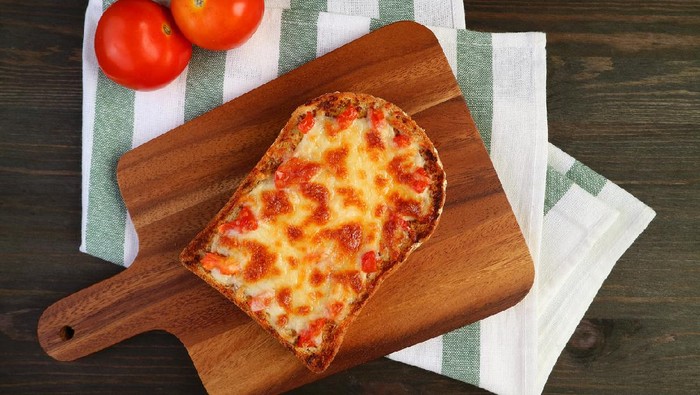 Top view of fresh baked homemade pizza toast on breadboard with fresh tomatoes on kitchen cloth