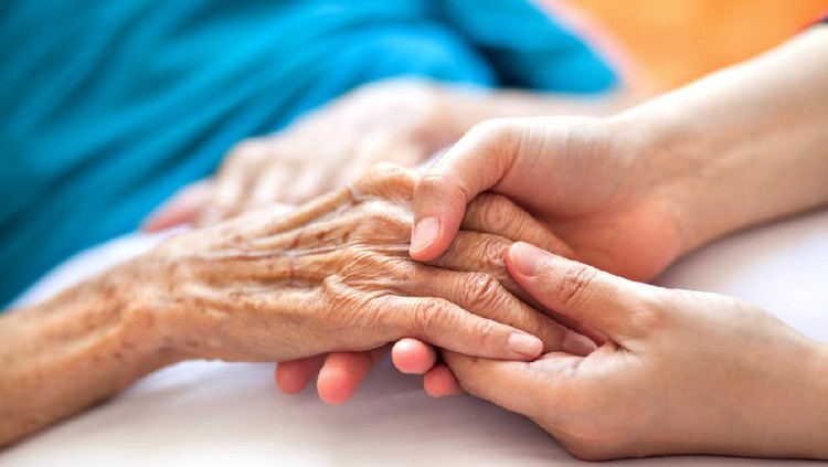 Woman holding senior woman's hand on bed