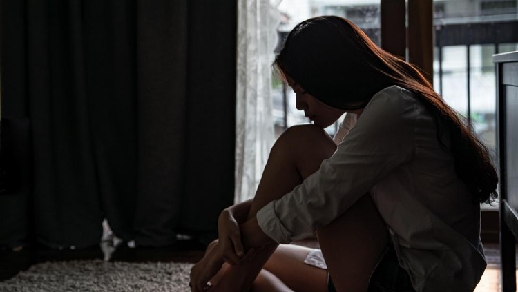 1173052440 Selective focus loneliness young asian woman sitting on bedroom floor near the balcony. Depression sadness breaking up asian teenage girl sitting alone hugging knees closing eyes and thinking.