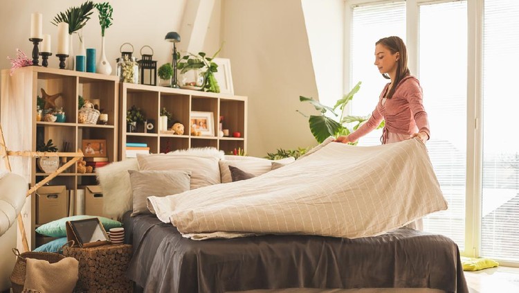 Young woman making bed in her bedroom in the morning.