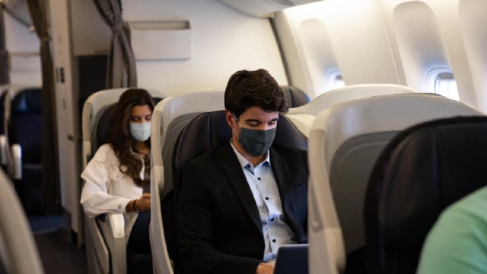 Business man traveling and wearing a facemask on the plane while using his laptopâ COVID-19 pandemic lifestyle concepts