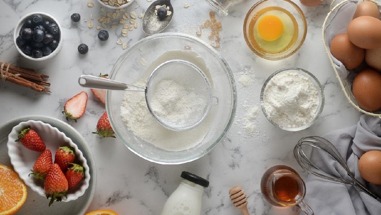 Making pancakes, cake, baking of baker hands pouring or sifting flour in bowl. Concept of Cooking ingredients and method on white marble background. Dessert recipes and homemade.