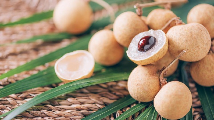 kelengkeng Longan fruits over palm leaves on rattan background. Copy space. Dimocarpus longan. Bunch of exotic longans. Tropical food concept