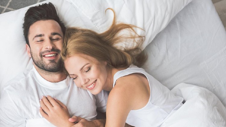 I am so happy with you. Top view portrait of cheerful young man and woman embracing while lying on bed. They are smiling with closed eyes