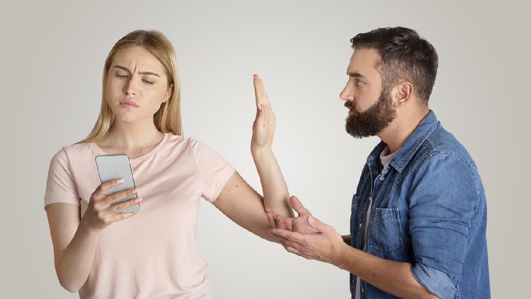 ilustrasi pasangan Family problems, indifference and quarrel. Busy young wife looking at phone, typing message and making stop hand gesture for husband, want to talk isolated on gray background, free space, studio shot