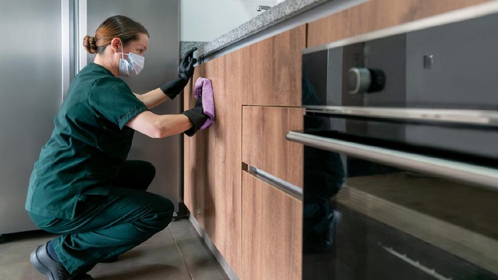 Latin American cleaner wearing a facemask while cleaning the kitchen at a house during the COVID-19 pandemic