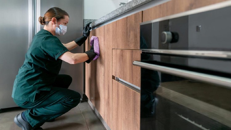 Latin American cleaner wearing a facemask while cleaning the kitchen at a house during the COVID-19 pandemic