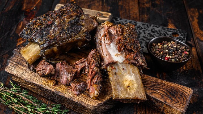 BBQ short chuck beef ribs with herbs and meat cleaver. Dark wooden background. Top view.