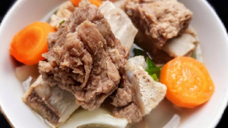 sop iga Close up of sop iga or beef short ribs soup in a white bowl on black background. Indonesian beef short ribs soup with carrot, cabbage, and spring onion. Meat and vegetable soup in a white bowl