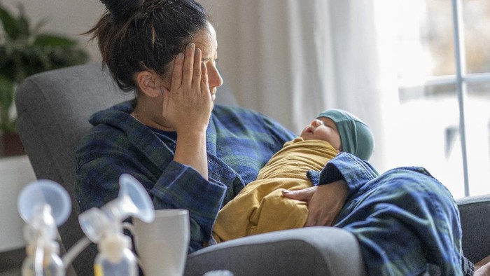 Tired mother holding her newborn child at home after tying to pump.