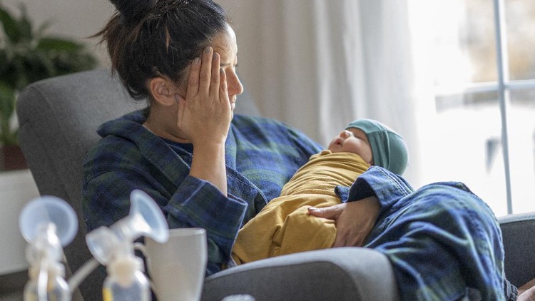 ibu menyusui stres Tired mother holding her newborn child at home after tying to pump.