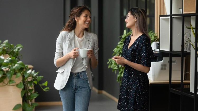 Asian and Caucasian ethnicity women colleagues met in office hall chatting enjoy friendly warm conversation, multi-ethnic mates having informal talk drink tea or coffee take break distracted from work