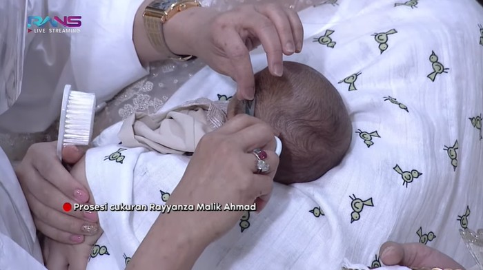 Selain pemotongan dua ekor kambing yang telah dilaksanakan secara terpisah, ada juga prosesi utama yakni cukuran rambut Rayyanza. Di prosesi ini, keluarga besar ikut memotong rambut putra Raffi dari Mamah Rieta sampai dengan Mamah Dedeh. Nantinya, rambut dari hasil cukuran akan ditimbang dan beratnya dikonversi ke harga emas untuk selanjutnya disedekahkan. (Foto: Screenshoot YouTube/Rans Entertainment)