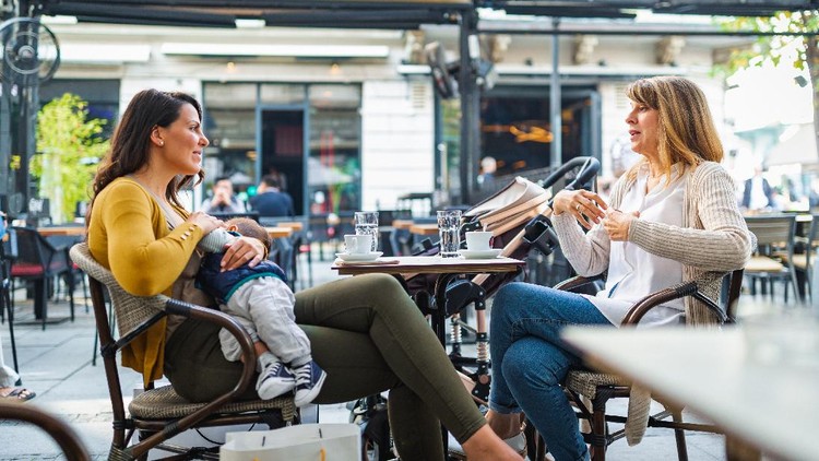 Young mother breastfeeding her baby boy in public while sitting in a cafe with her mother
