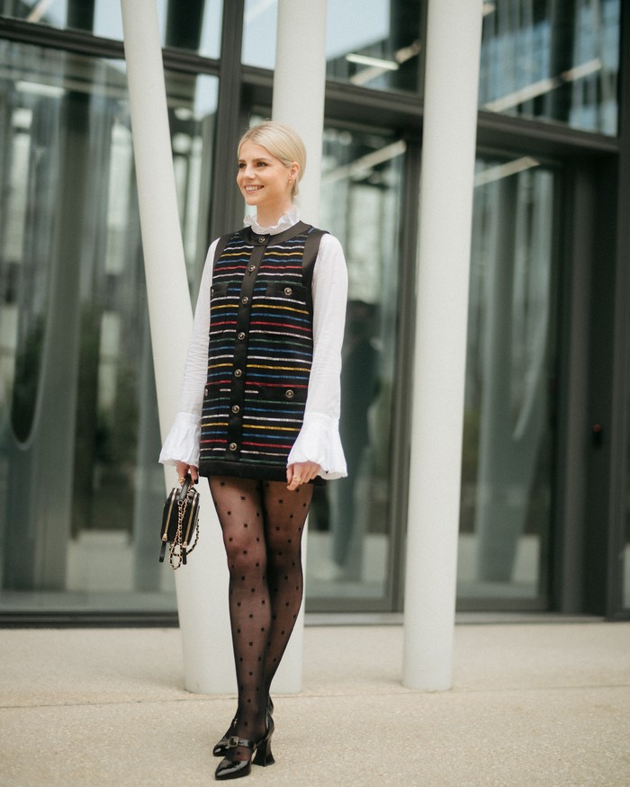 Aktris Lucy Boynton tampil dalam padanan bergaya preppy lewat perpaduan dress multiwarna dari koleksi busana siap pakai Chanepl spring/summer 2022 dan kemeja putih. Foto: Courtesy of Chanel