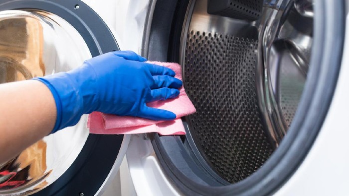 Hand in blue glovesw cleaning washing mashine with piece of cloth