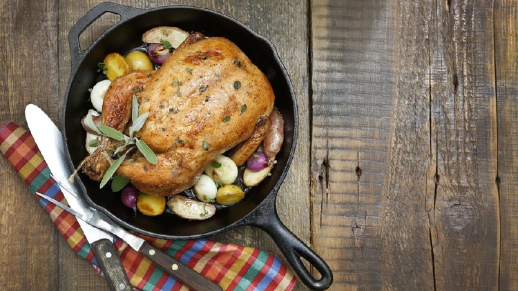 A overhead view of a roast chicken on a rustic wood table top.