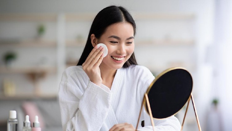 Beautiful asian woman cleaning her face, using cotton pads and cleansing product, looking at mirror in bedroom. Young attractive korean lady using face toner and cotton pad, home interior, empty space