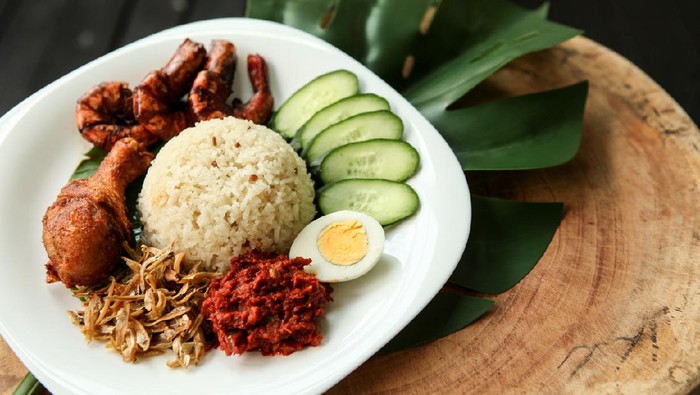 Nasi lemak or fragrant rice dish cooked in coconut milk and pandan leaf, commonly found in Malaysia and considered as the national dish. It is also a native dish in neighbouring countries with significant Malay population. Image shows nasi lemak with fried chicken, hard boiled egg, sambal, anchovies, sliced cucumber, marinated fried prawn. It is traditionally served with cut banana leaf spread or wrapped in it.