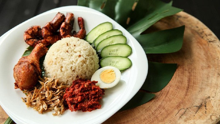 Nasi lemak or fragrant rice dish cooked in coconut milk and pandan leaf, commonly found in Malaysia and considered as the national dish. It is also a native dish in neighbouring countries with significant Malay population. Image shows nasi lemak with fried chicken, hard boiled egg, sambal, anchovies, sliced cucumber, marinated fried prawn. It is traditionally served with cut banana leaf spread or wrapped in it.