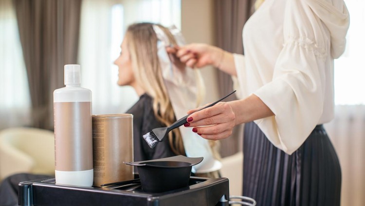 mewarnai rambut Blonde woman dyeing her hair at the salon. She is sitting and the hairdresser/hairstylist is putting hair color on her hair. This is regular hair care treatment in customers favorite salon.