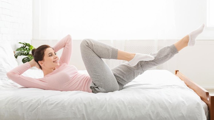 olahraga di rumah Morning fitness. Sporty lady doing fit exercises, lying on bed at home, panorama