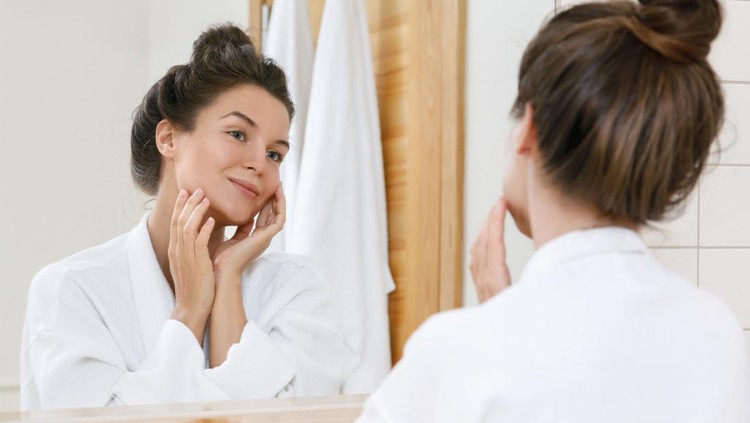 Young woman is looking into the mirror at morning