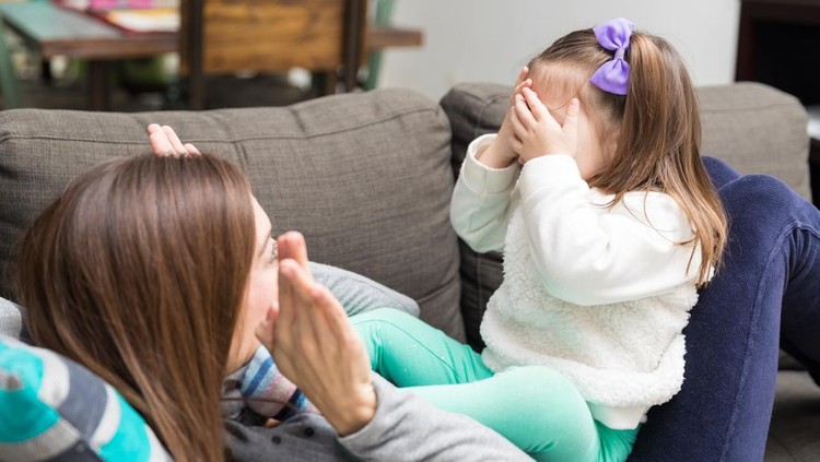 Joyful mid adult mother and cute daughter playing peekaboo on sofa at home