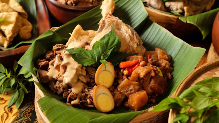 gudeg Gudeg Jogja, a Javanesse signature dish of young jackfruit stew; accompanied with white chicken curry and spicy stew of cattle skin cracker. All the dishes are arranged in a bamboo basket as a take-out container. In the background is each of the individual dish that makes up Gudeg Jogja.