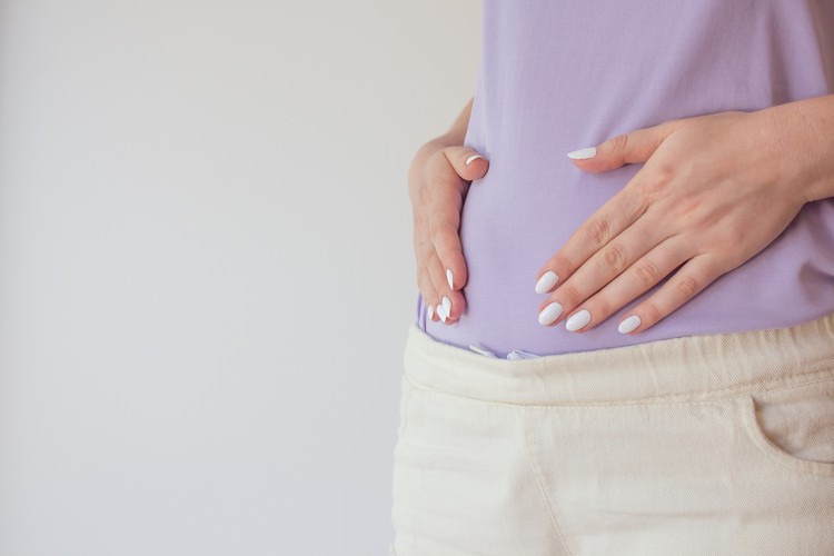 hamil muda Pregnant woman in the early stages touches the belly with her hands. First and second trimester of pregnancy.