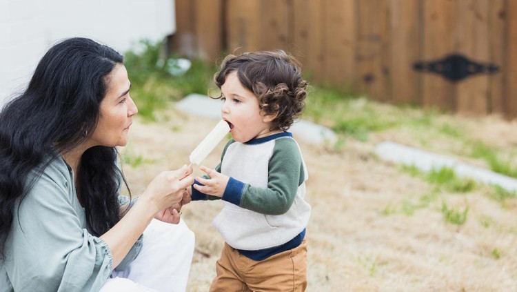 es krim Sitting outside in their yard, the mature adult grandmother gives her toddler grandson a taste of a frozen ice.